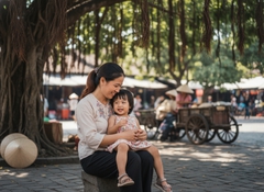 1 bé gái ngồi trên người mẹ . Với đặc điểm phong cách thực...